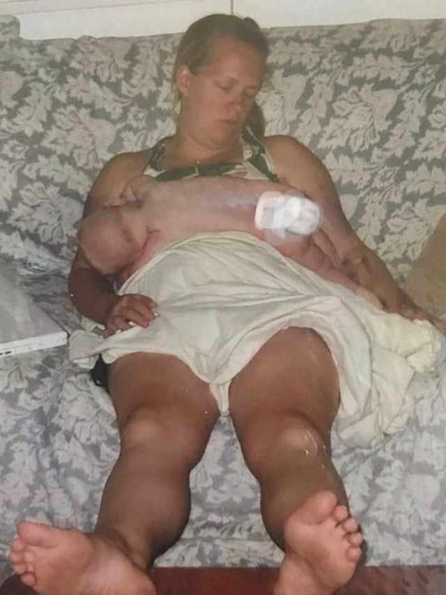 Woman fast asleep sitting up with a baby on her chest.