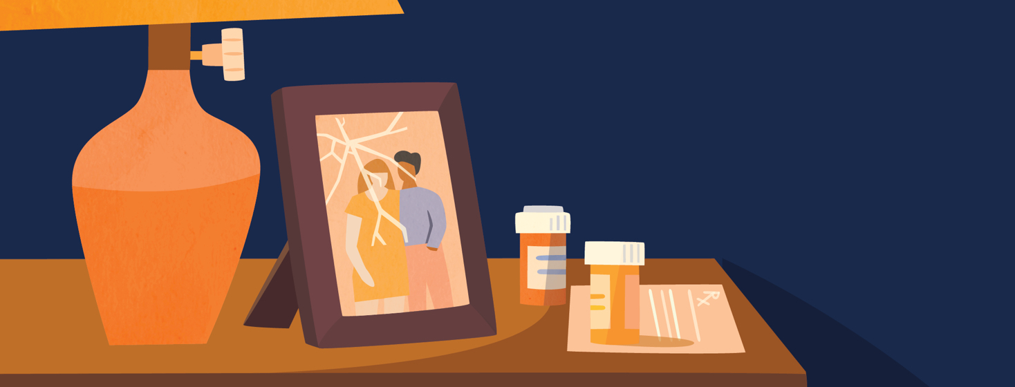 a table with a lamp, a broken picture frame showing a couple, and pill bottles sitting on top of a prescription