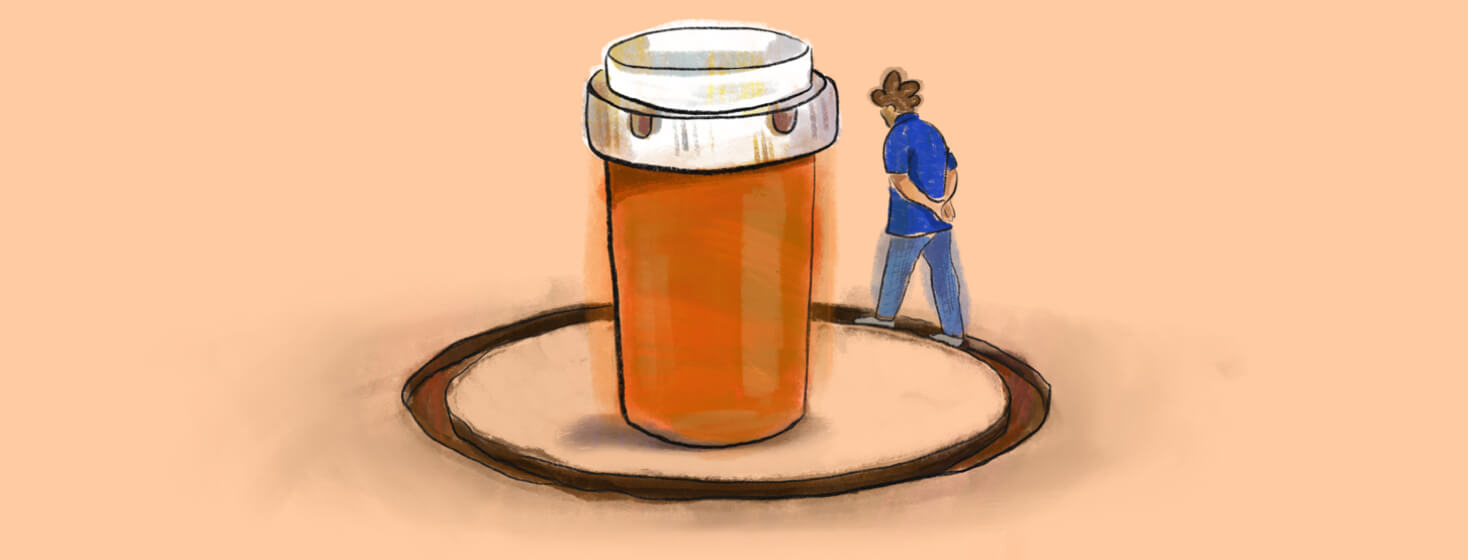 A person walks in a worn down path around a large prescription medicine bottle
